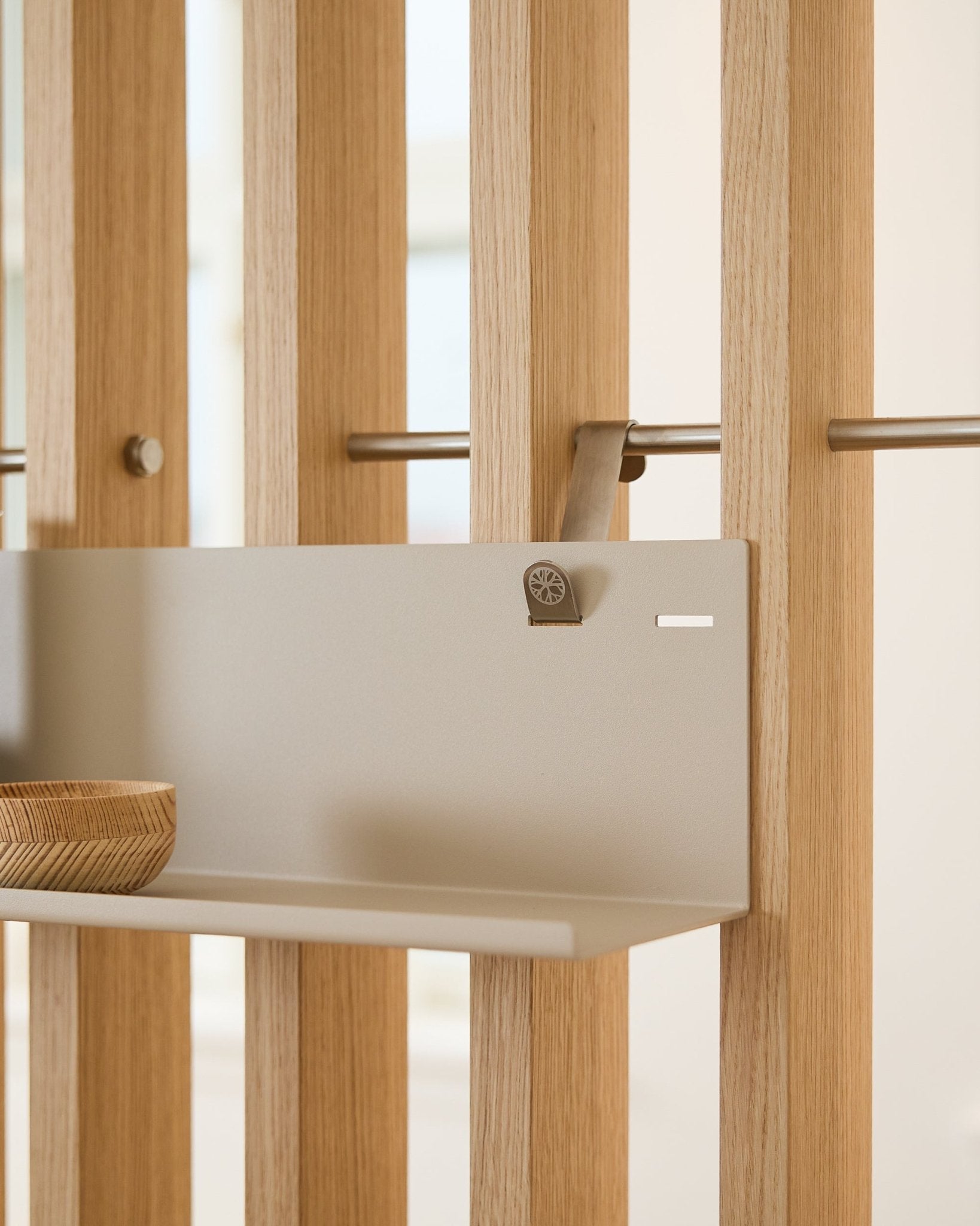 Beige WoodUpp BM1 metallhylle (63 x 13,4 cm) montert på vertical akustisk spileveggpanel, med en treskål på venstre side av hyllen.