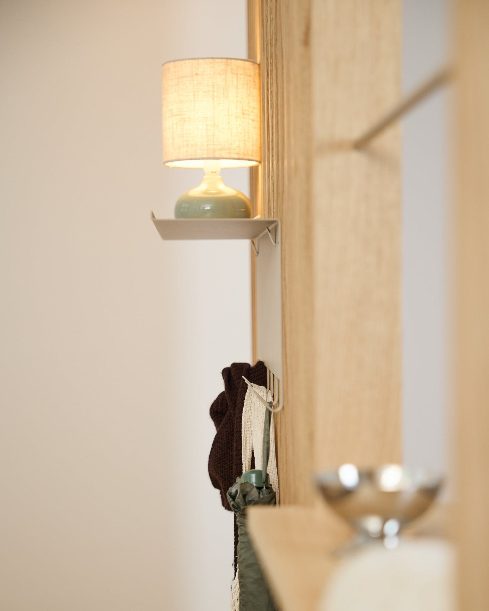 En beige WoodUpp Nell knaggrekke BM1 (63,5 x 24 cm) står under en small bordlampe ved siden av en vegg i lyst nordisk tre Akustikkpanel.