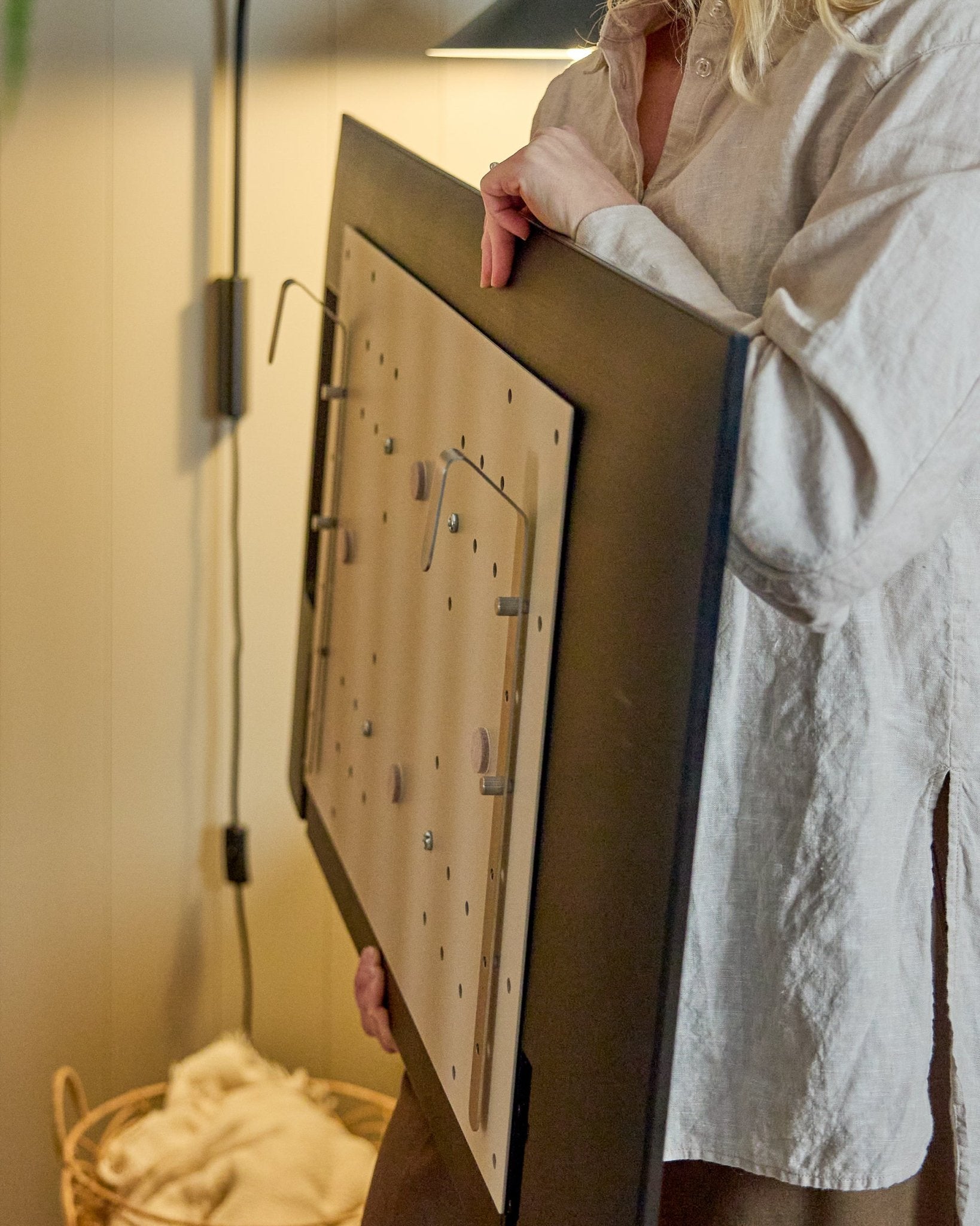 En person i en lys skjorte holder WoodUpp Nell BM1 TV-Mount i beige, 64x44 cm—kompatibel med nordiske akustiske trepaneler, for installasjoner uten vegg.