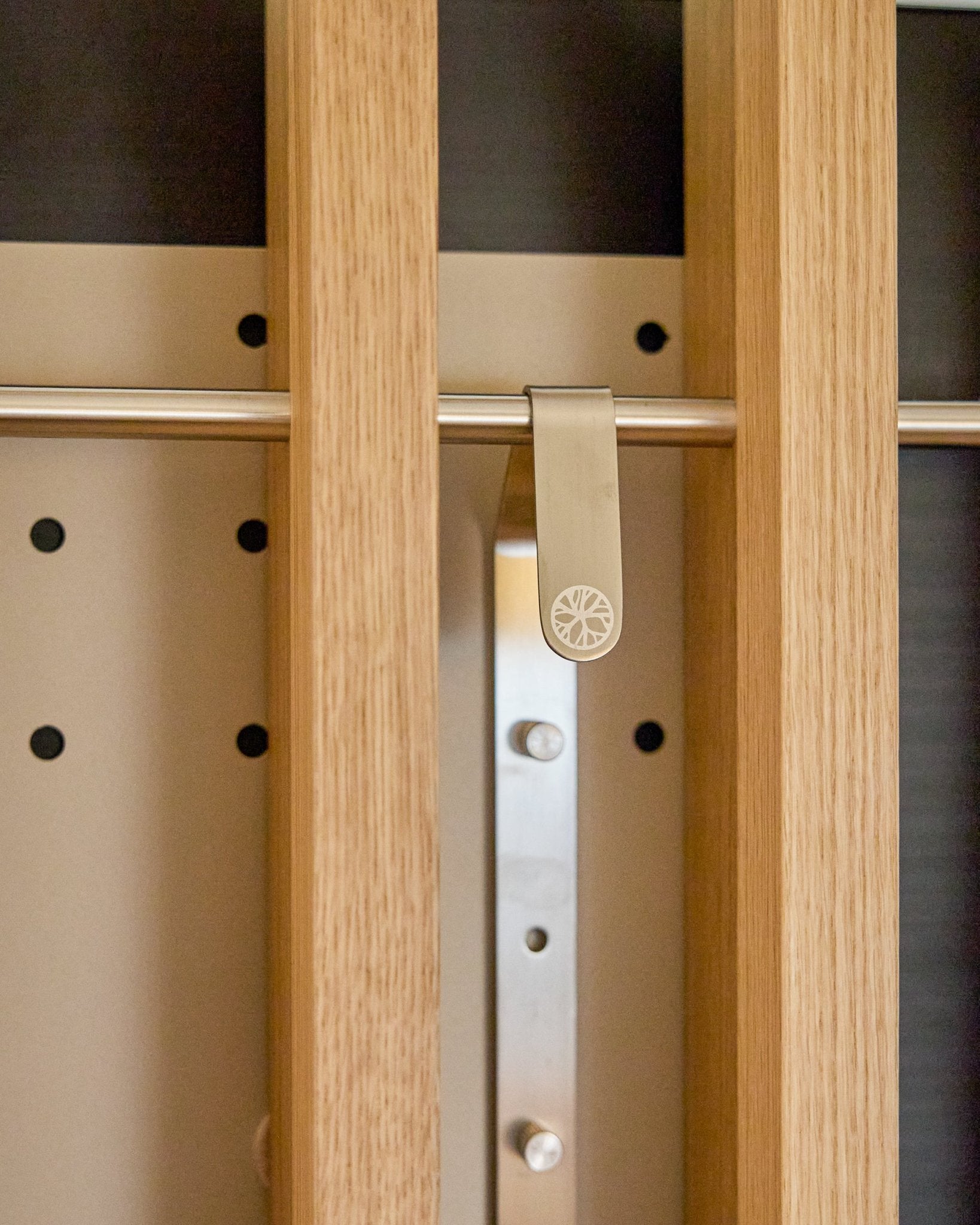 En metallisk solstråleformet klips festet til en trespile på WoodUpp Nell | TV-Mount BM1, Beige, 64x44 cm Akustikkpanel skap med høydejustering.