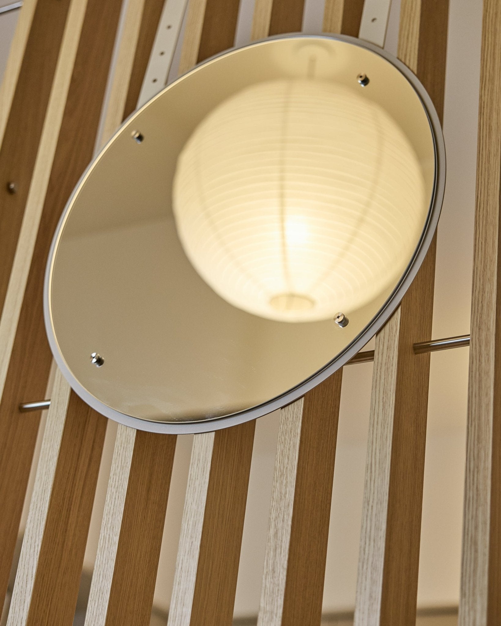 Vala | Mirror / BM1, D54 cm fra WoodUpp er et høydejusterbart rundt speil montert på vertical akustiske spilepaneler som reflekterer en glødende papirlampe.