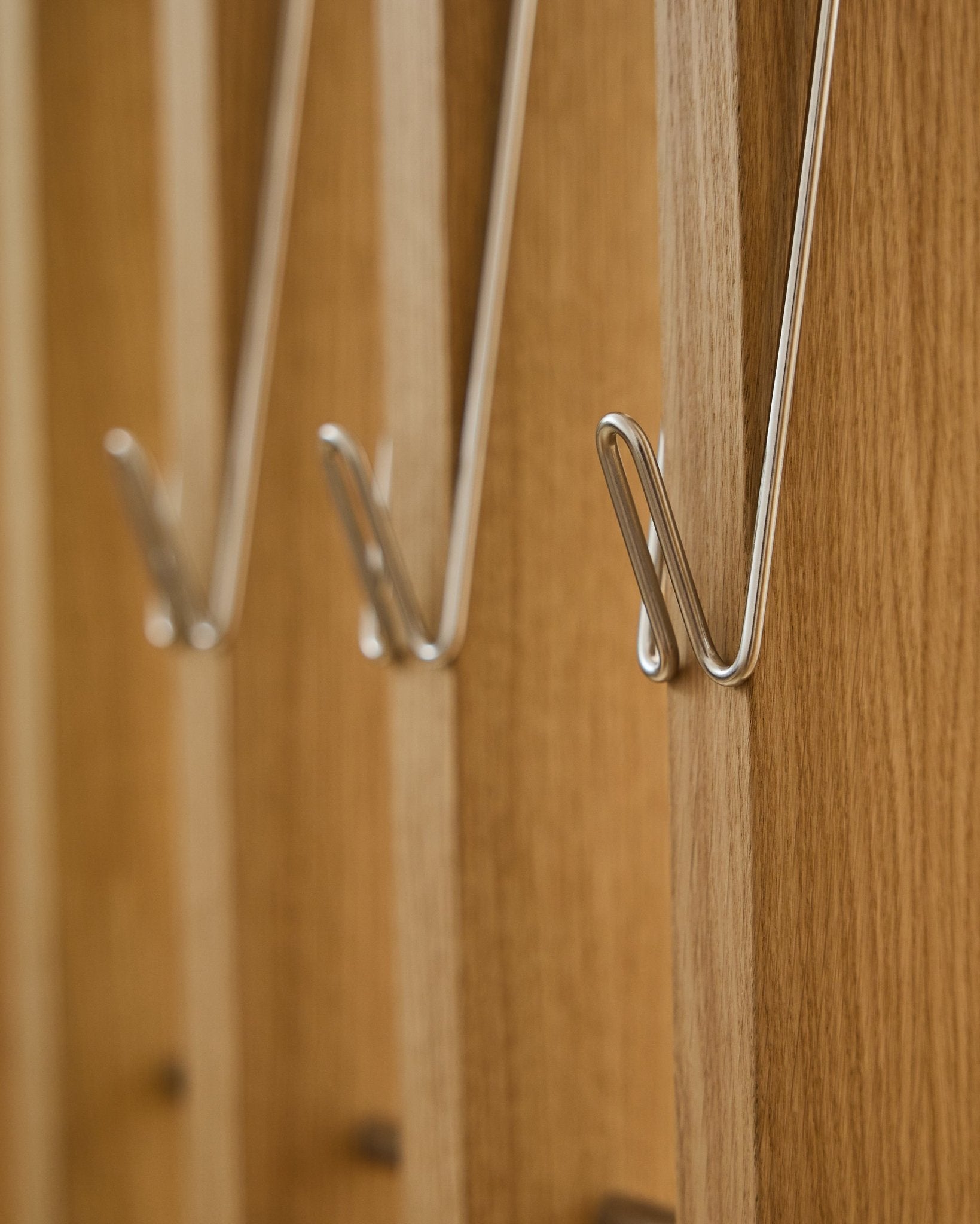 Nærbilde av tre Alva | Wire Hook / BM1, rustfritt Steel, lang fra WoodUpp, montert på rekke på Akupanel akustiske trepaneler og som kaster myke skygger.