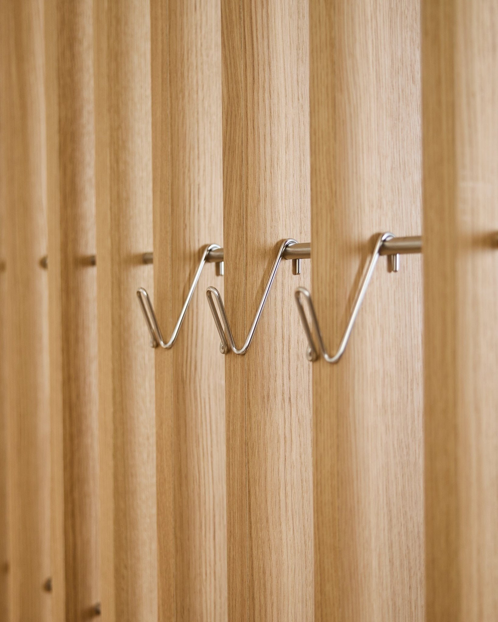 Tre korte Alva Wire Hook / BM1-tilbehør i rustfritt steel fra WoodUpp er montert jevnt på rekke på et vertical akustisk spilepanel i tre.