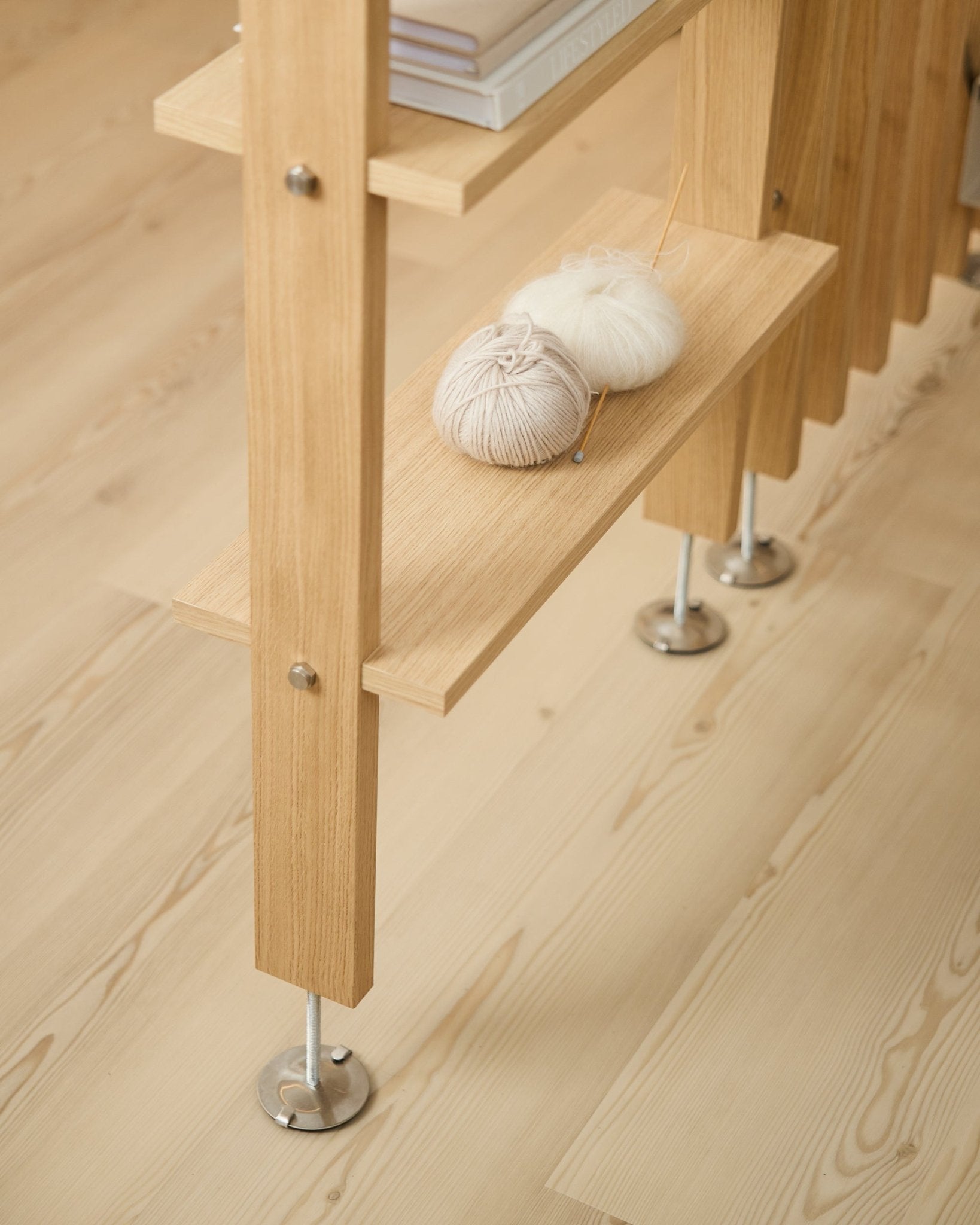 Lova | Wood Shelf / BM2 fra WoodUpp i eikefiner (65,8 x 20 cm), med garn og strikkepinner på den nederste hyllen, på et lyst tregulv med metallføtter.