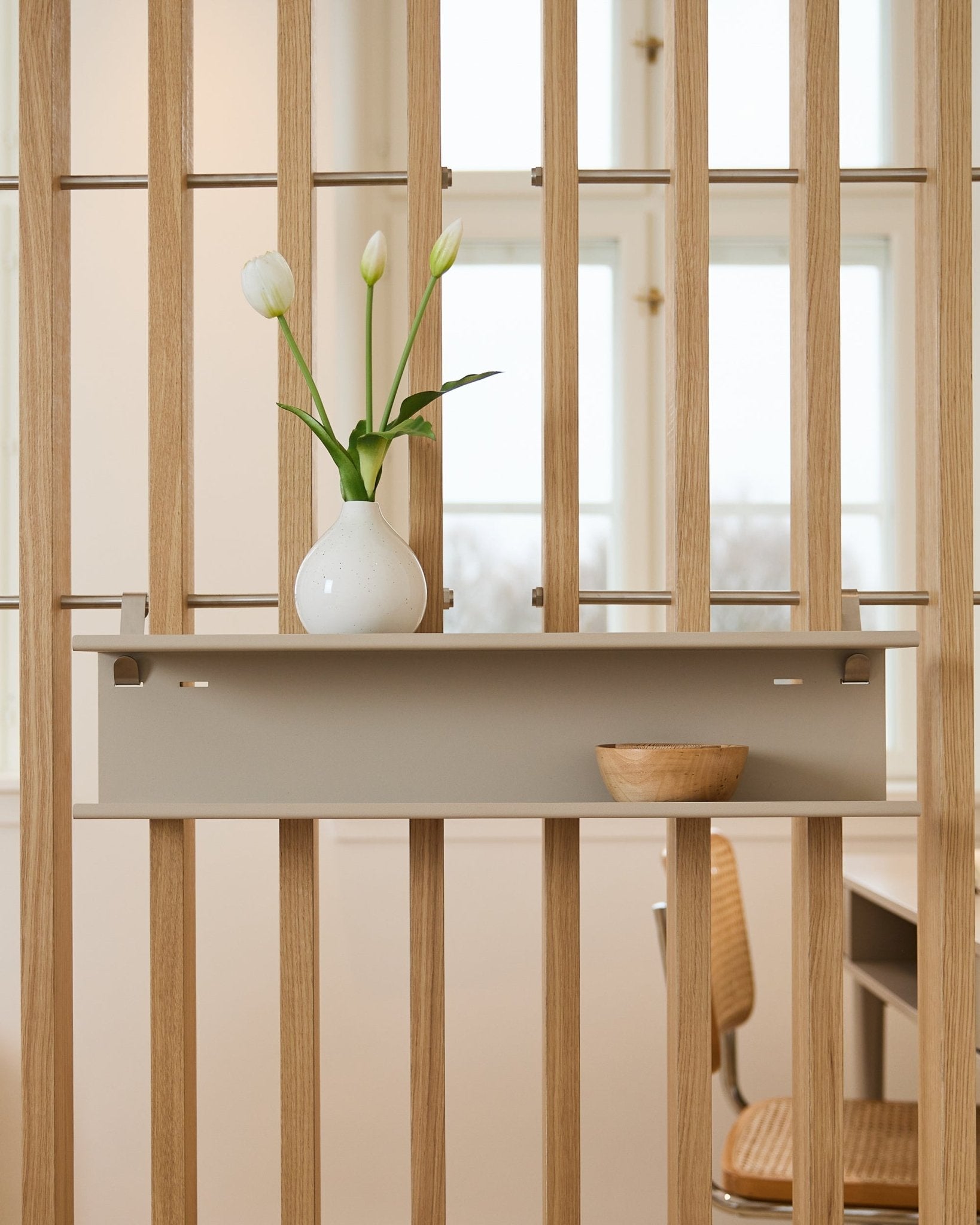 Double Metal Shelf / BM1 fra WoodUpp i beige (63,5 cm) montert på en spile-romdeler, stylet med en vase og en treskål.