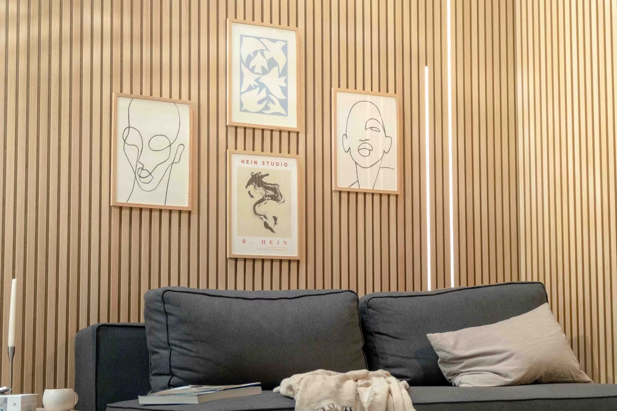Modern living room featuring a dark sofa with a beige pillow, accented by a Nordic Akupanel acoustic wood slat wall and minimalist Scandinavian art above.
